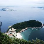 Vista aérea da costa do Rio de Janeiro, com mar, áreas verdes e trechos urbanizados.