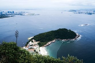 Vista aérea da costa do Rio de Janeiro, com mar, áreas verdes e trechos urbanizados.