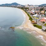 Vista aérea de uma cidade costeira com faixa de areia junto ao mar e ondas alcançando a praia.