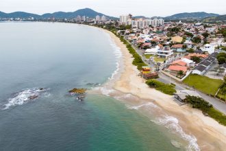 Vista aérea de uma cidade costeira com faixa de areia junto ao mar e ondas alcançando a praia.