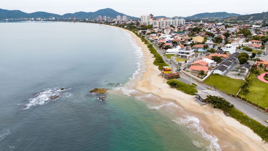 Vista aérea de uma cidade costeira com faixa de areia junto ao mar e ondas alcançando a praia.
