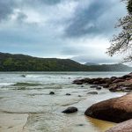 Praia da Enseada, em Ubatuba, com águas calmas, faixa de areia e morros cobertos de vegetação.
