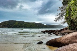 Praia da Enseada, em Ubatuba, com águas calmas, faixa de areia e morros cobertos de vegetação.