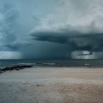 Praia arenosa com ondas agitadas e nuvens carregadas indicando a aproximação de uma tempestade.