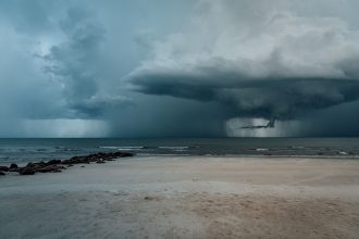 Praia arenosa com ondas agitadas e nuvens carregadas indicando a aproximação de uma tempestade.