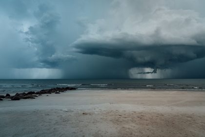 Praia arenosa com ondas agitadas e nuvens carregadas indicando a aproximação de uma tempestade.