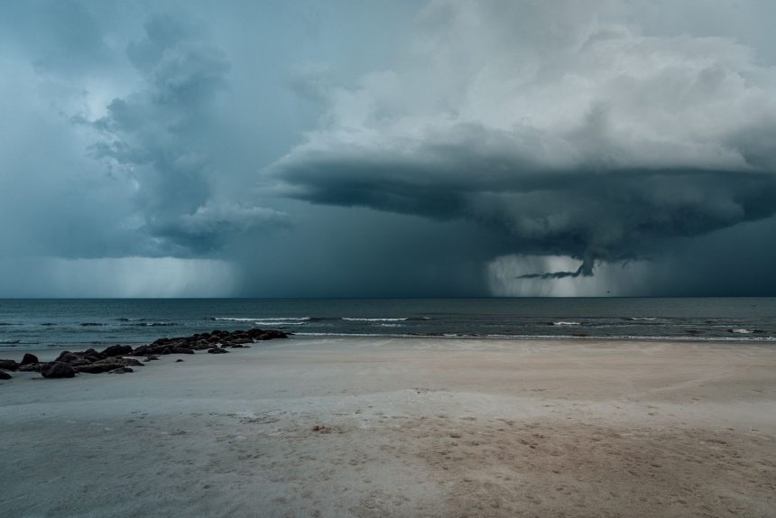 Praia arenosa com ondas agitadas e nuvens carregadas indicando a aproximação de uma tempestade.